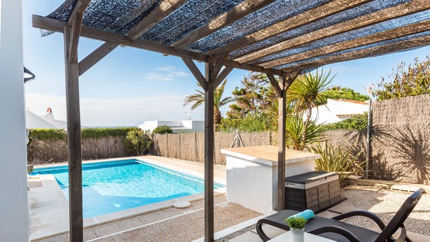 A covered outdoor area with a pool, seating, and a small table with a plant.