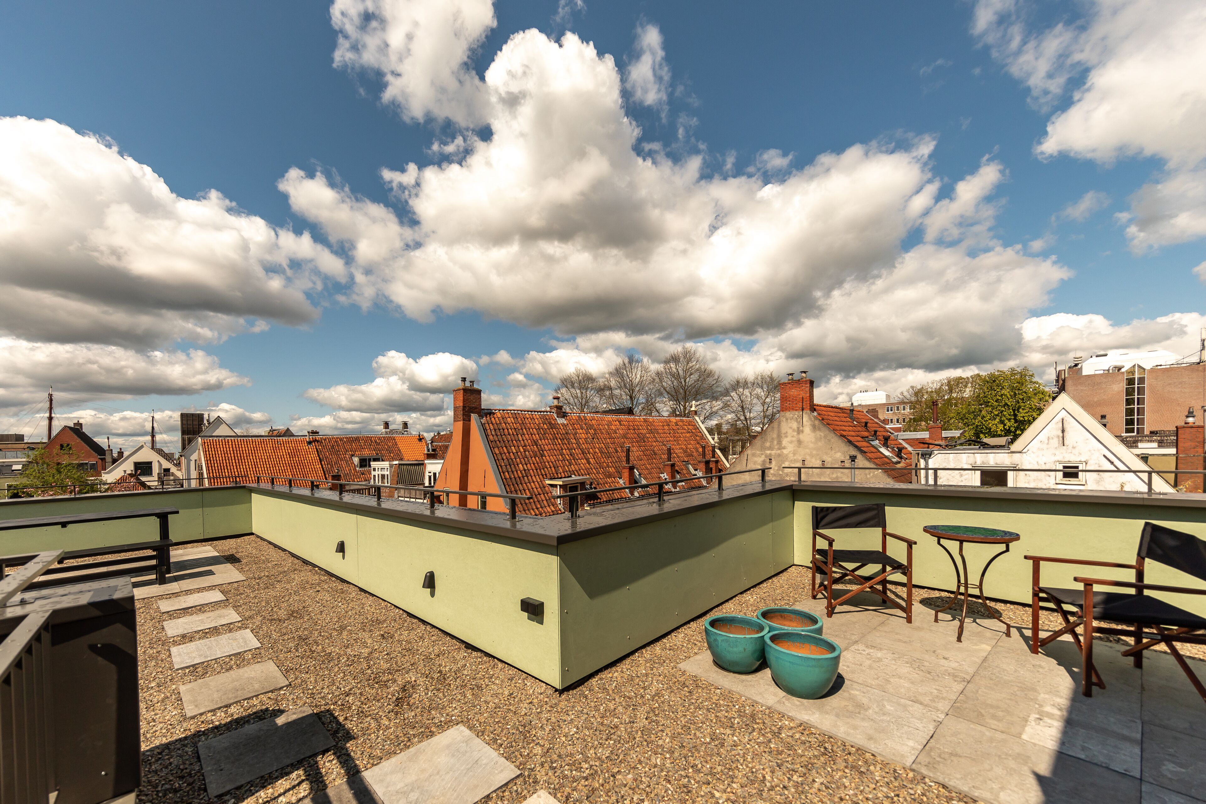 A rooftop terrace with a green wall, a wooden deck, and a seating area with chairs and a table.