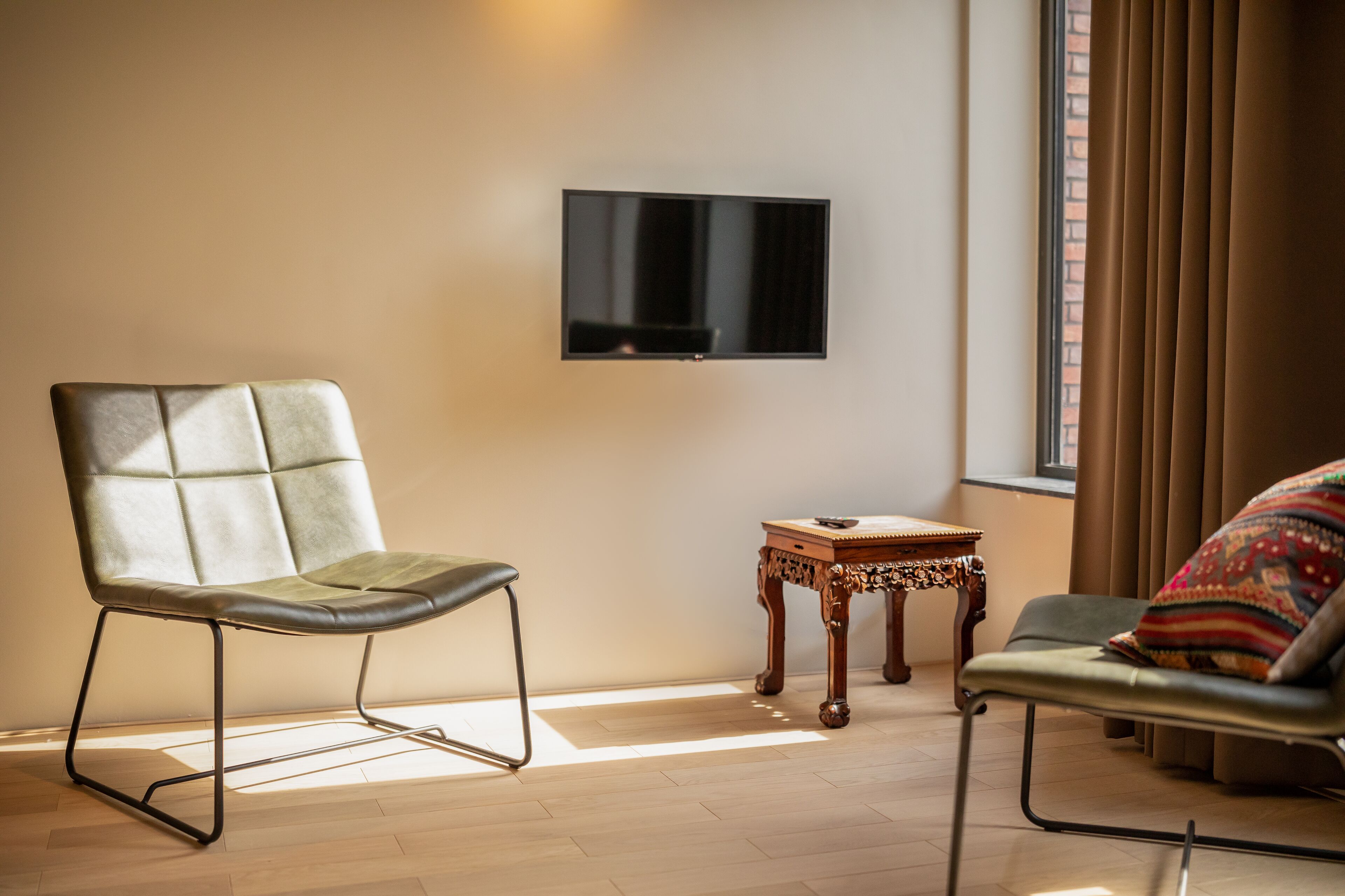 A modern living room with a leather chair, a small wooden table, and a flat-screen TV mounted on the wall.