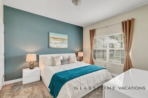 Een slaapkamer met een bed, nachtkastjes, een raam met gordijnen en een schilderij aan de muur.