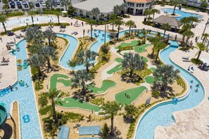 Luchtbeeld van een resort met meerdere zwembaden, palmbomen en een groot gebouw op de achtergrond.
