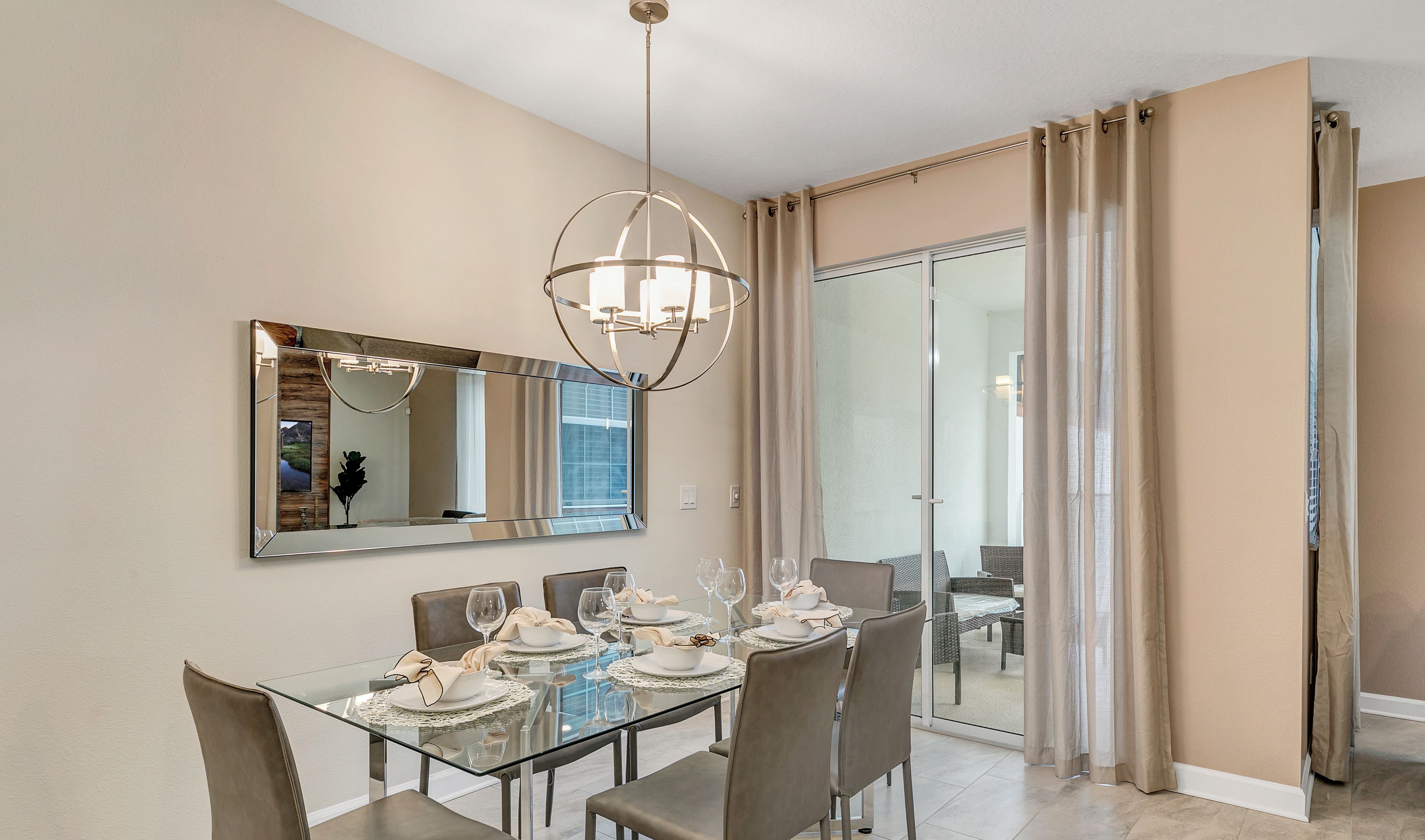 Un coin repas avec une table en verre, des chaises et un lustre. Un grand miroir orne le mur, et une porte-fenêtre coulissante donne accès à une autre pièce.
