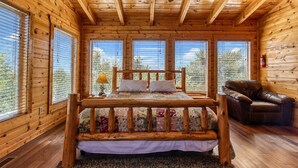 Camera da letto in una baita di legno con un letto di legno, una poltrona in pelle e una ventola a soffitto.