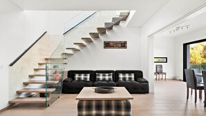 A modern living room with a glass staircase, a black sofa set, and a wooden coffee table. - Villa Caterina - Playa de Punta Prima (San Luis)