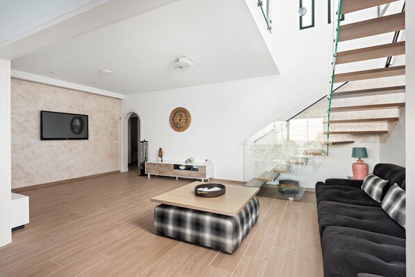 Ein modernes Wohnzimmer mit Holzboden, einer schwarzen Couch, einem Couchtisch und einer Treppe mit Glastrennläufen.