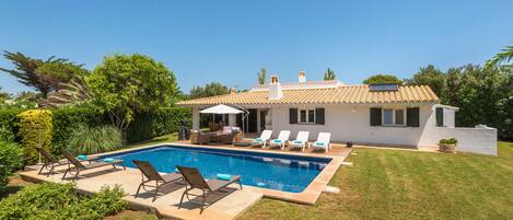 A modern house with a swimming pool, outdoor furniture, and a well-maintained lawn.