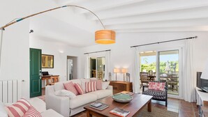 A living room with a sofa, coffee table, and a television. There is a door leading to a balcony with a view of greenery. - Villa Sirena - Cap den Font (San Luis)