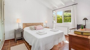 A bedroom with a bed, bedside tables, a window with curtains, and a view of greenery outside. - Villa Sirena - Cap den Font (San Luis)