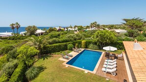 A rectangular swimming pool with lounge chairs and umbrellas, surrounded by lush greenery and a view of the sea. - Villa Sirena - Cap den Font (San Luis)