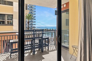 A balcony with a view of the sea, a palm tree, and a building with balconies.