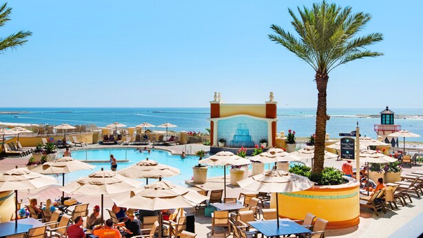 Área de piscina en un resort con sillones de descanso, sombrillas y vista al océano.