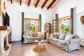 Amplia sala de estar con dos sofás, una chimenea y ventanas grandes con cortinas.