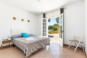 Ein Schlafzimmer mit Bett, Nachttisch, Stuhl und einer offenen Tür, die auf einen Balkon führt.