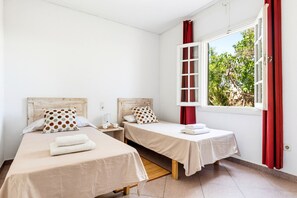 Ein Zimmer mit zwei Betten, einem Fenster mit roten Vorhängen und Blick auf Grünfläche.