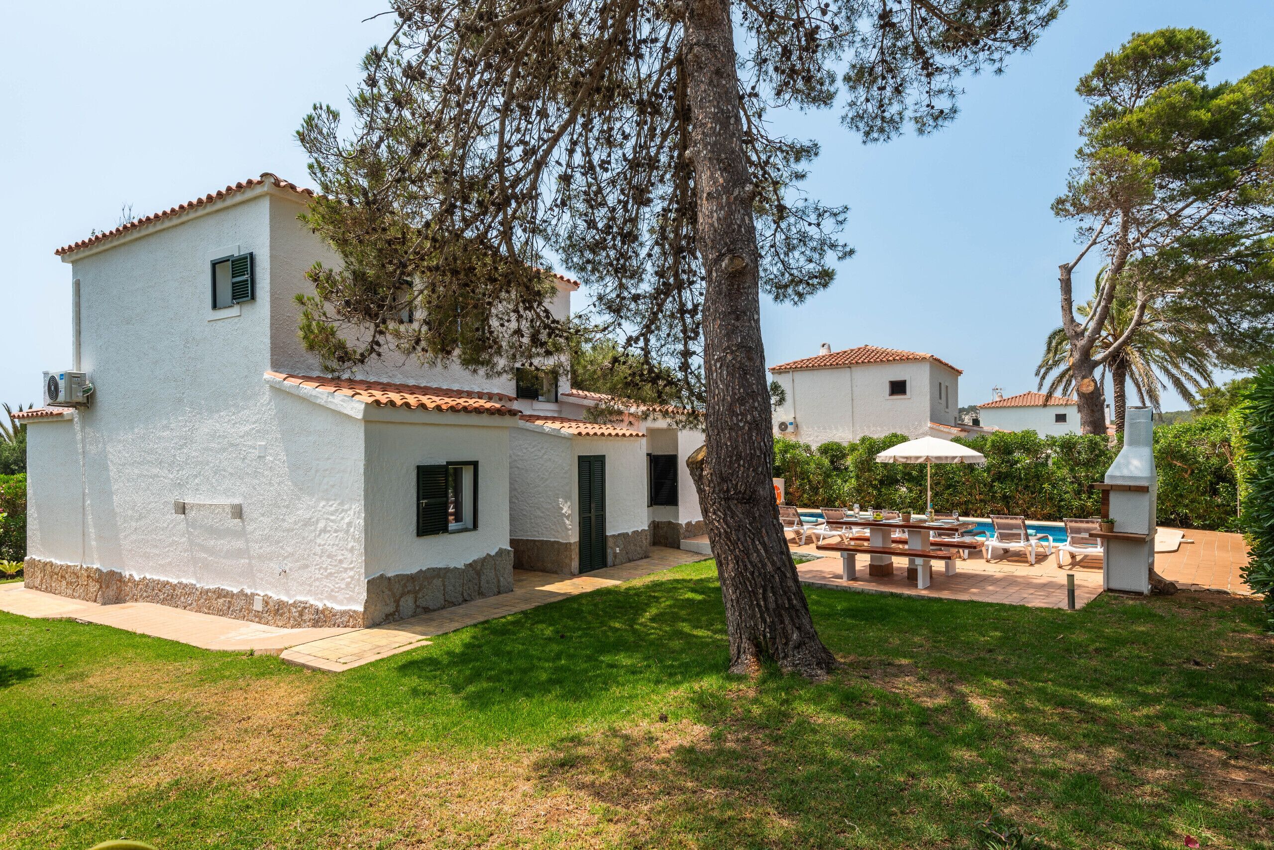 A white building with a tiled roof, a patio with outdoor furniture, and a pool area.
