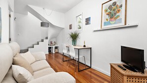 A modern living room with a sofa, a dining area with chairs, a TV on a wooden stand, and a staircase leading to another level. - Hort des Milord - Villa en Es Castell (Es Castell)