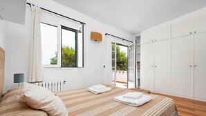 A modern bedroom with a large bed, a view of greenery outside, and a sliding door leading to a balcony. - Hort des Milord - Villa en Es Castell (Es Castell)