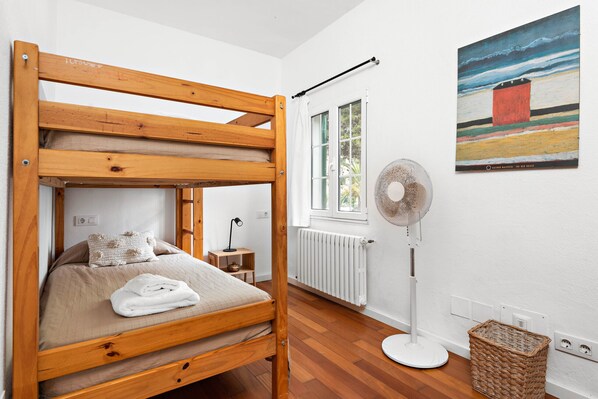 A bunk bed with a white blanket and pillow, a standing fan, a wicker basket, and a painting on the wall. - Hort des Milord - Villa en Es Castell (Es Castell)
