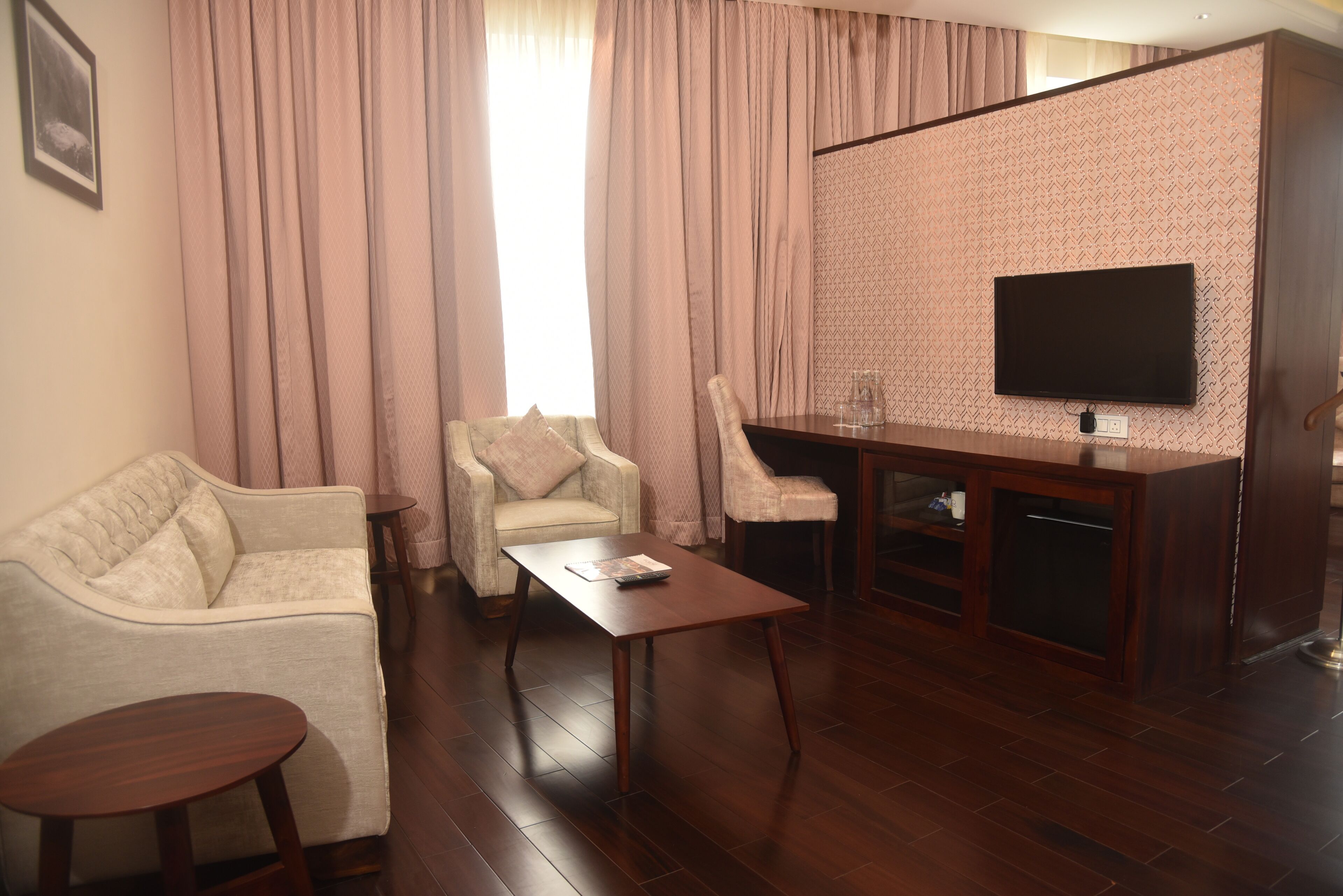 A living room with a sofa, two armchairs, a coffee table, and a TV mounted on a patterned wall.