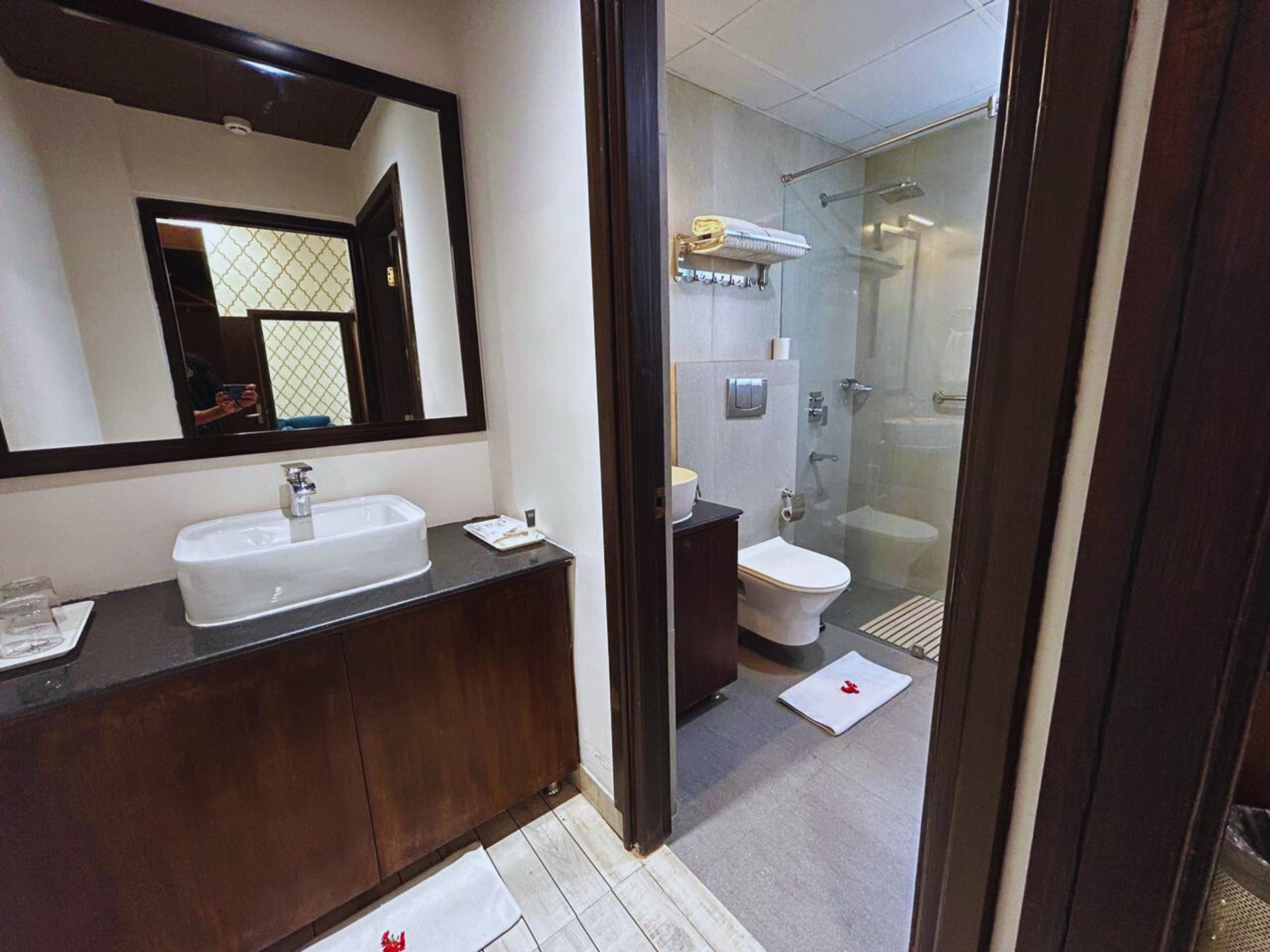 Een moderne badkamer met een grote spiegel, een witte wastafel, een toilet en een douchecabine met glazen wanden.