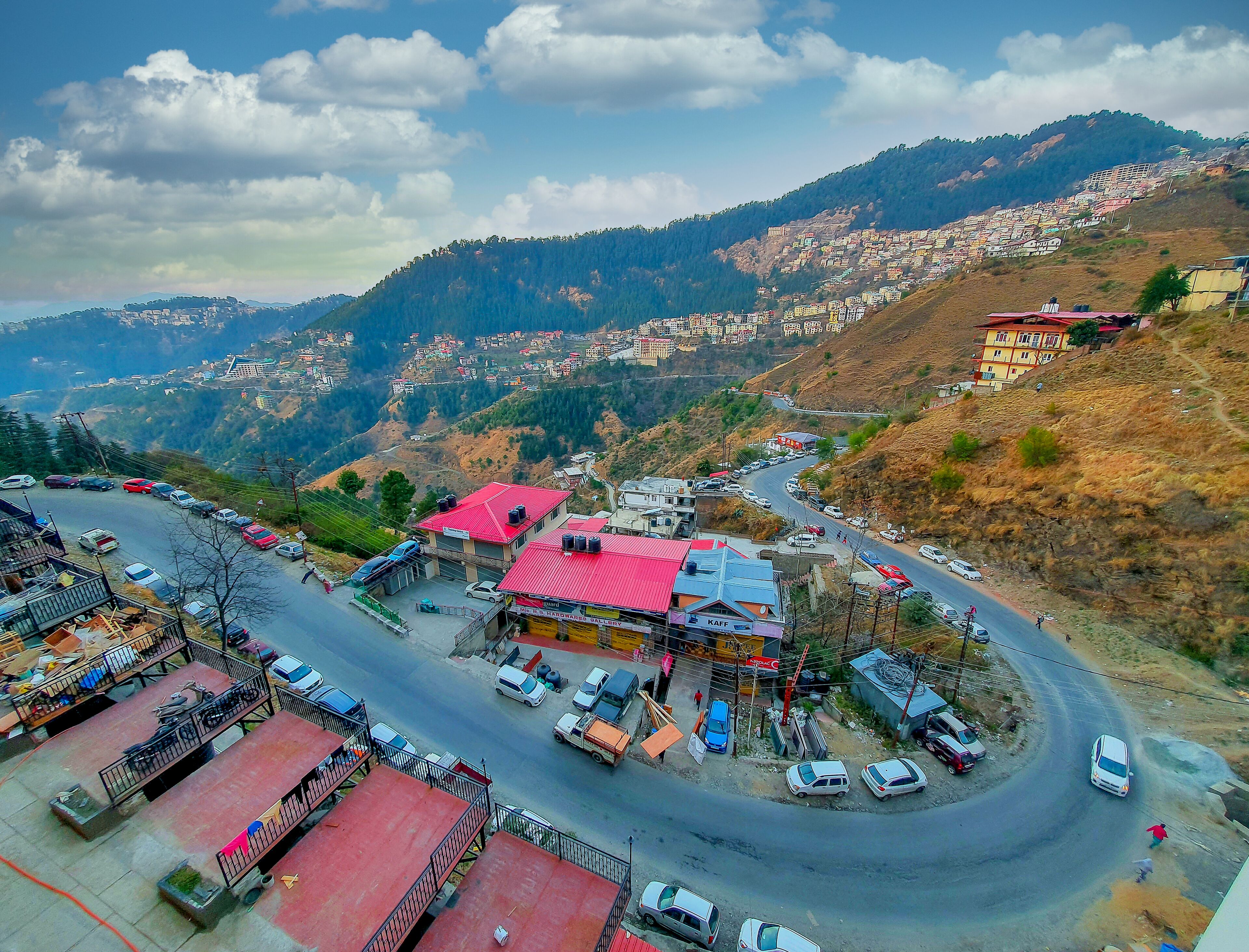 A hilly town with a winding road, buildings with red roofs, and a view of the surrounding mountains.
