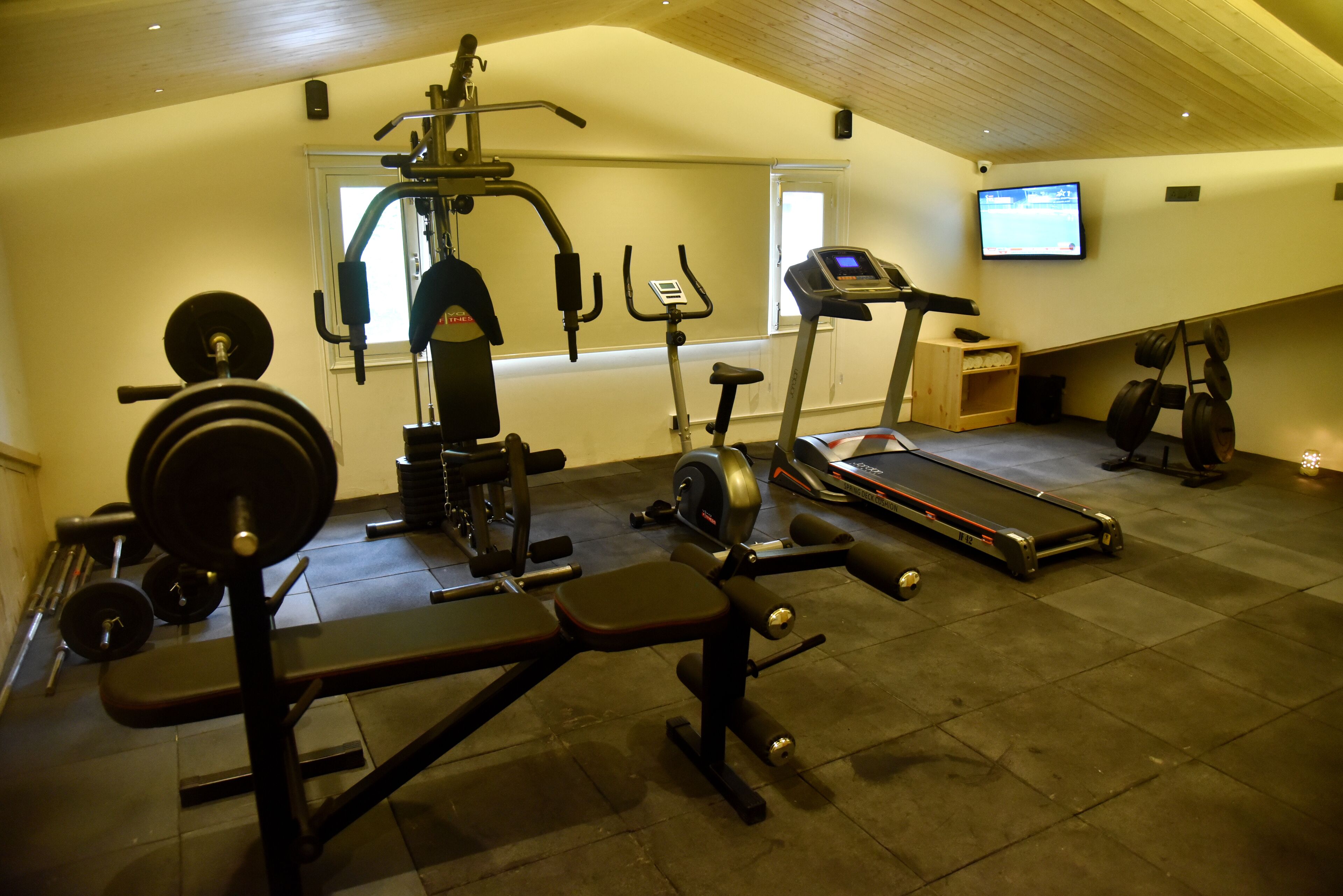 Ein Fitnessraum mit verschiedenen Trainingsgeräten, darunter ein Laufband, eine Gewichtbank und Gewichte.