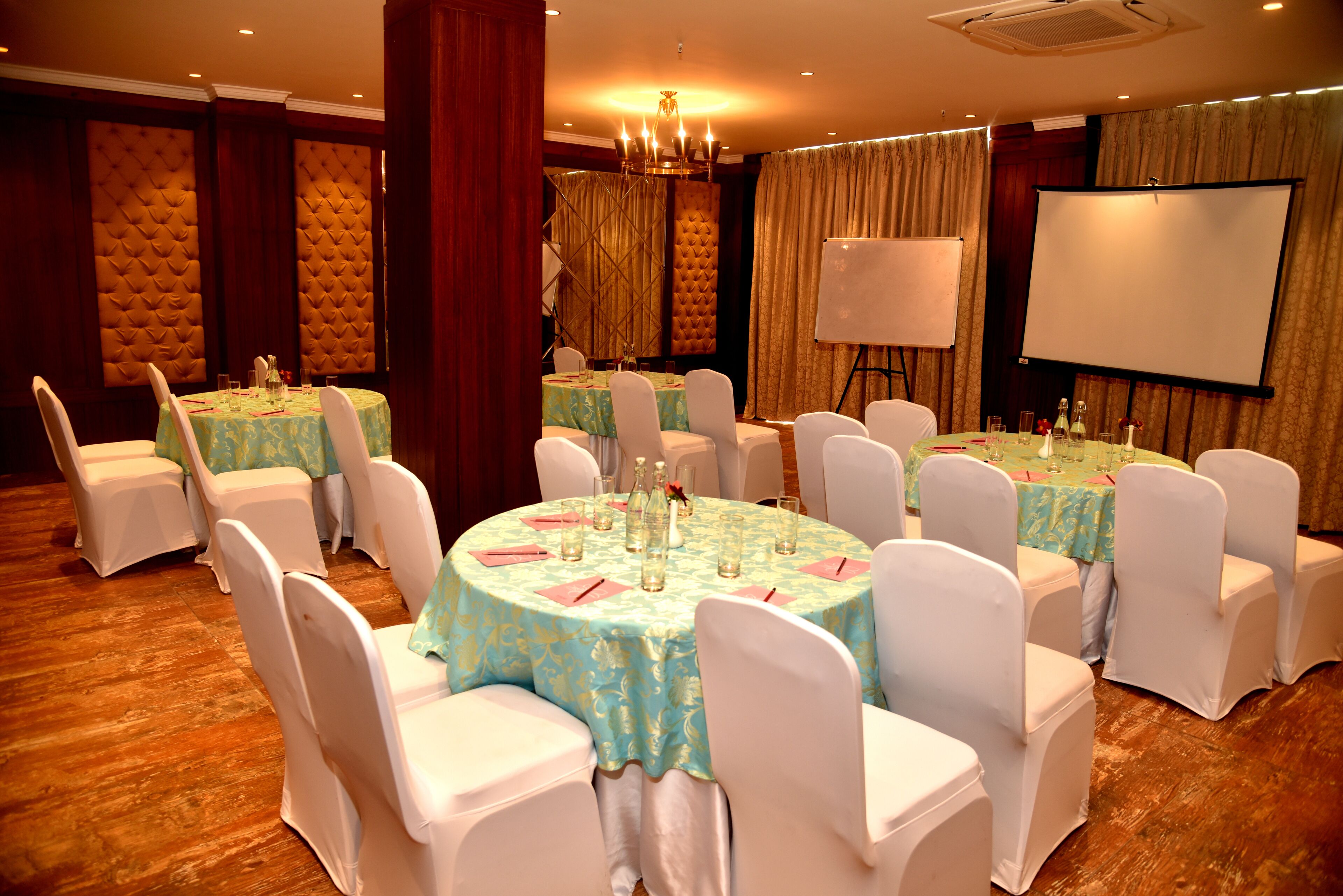 A banquet hall with round tables, white chairs, and a projector screen.