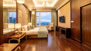 A spacious hotel room with a large bed, a sitting area with a chair, a wooden desk, and a television. - The Orchid Shimla (Shimla)