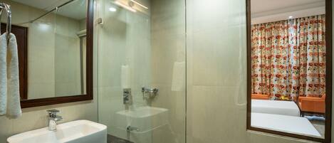A bathroom with a large mirror, a sink, and a shower.
