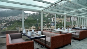 A restaurant with glass walls, offering a view of a hillside town. - The Orchid Shimla (Shimla)