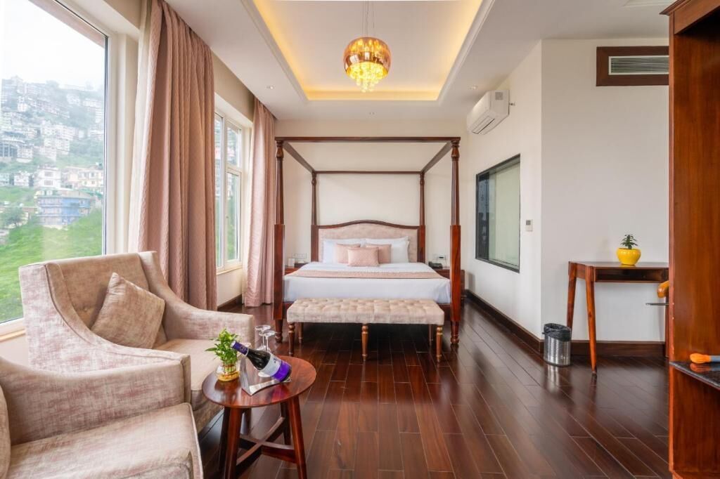 Een hemelbed met uitzicht op een stadsbeeld, een zithoek met een stoel en een klein tafeltje, en een houten vloer.