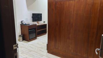 Una habitación con puerta de madera, televisor en la pared, un mueble pequeño y un cubo de basura.