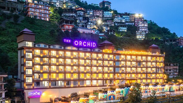 A hotel named "The Orchid" with multiple floors, a well-lit facade, and a view of surrounding hillside buildings. - The Orchid Shimla (Shimla)
