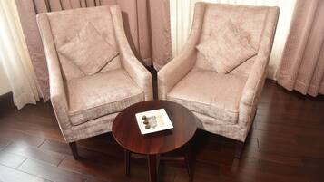 Dos sillones con una mesa redonda de madera en el centro, un plato con un adorno, y una ventana con cortinas translúcidas al fondo.