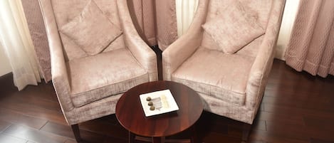 Two armchairs with a round wooden table between them, a plate with a decorative item, and a window with sheer curtains in the background.