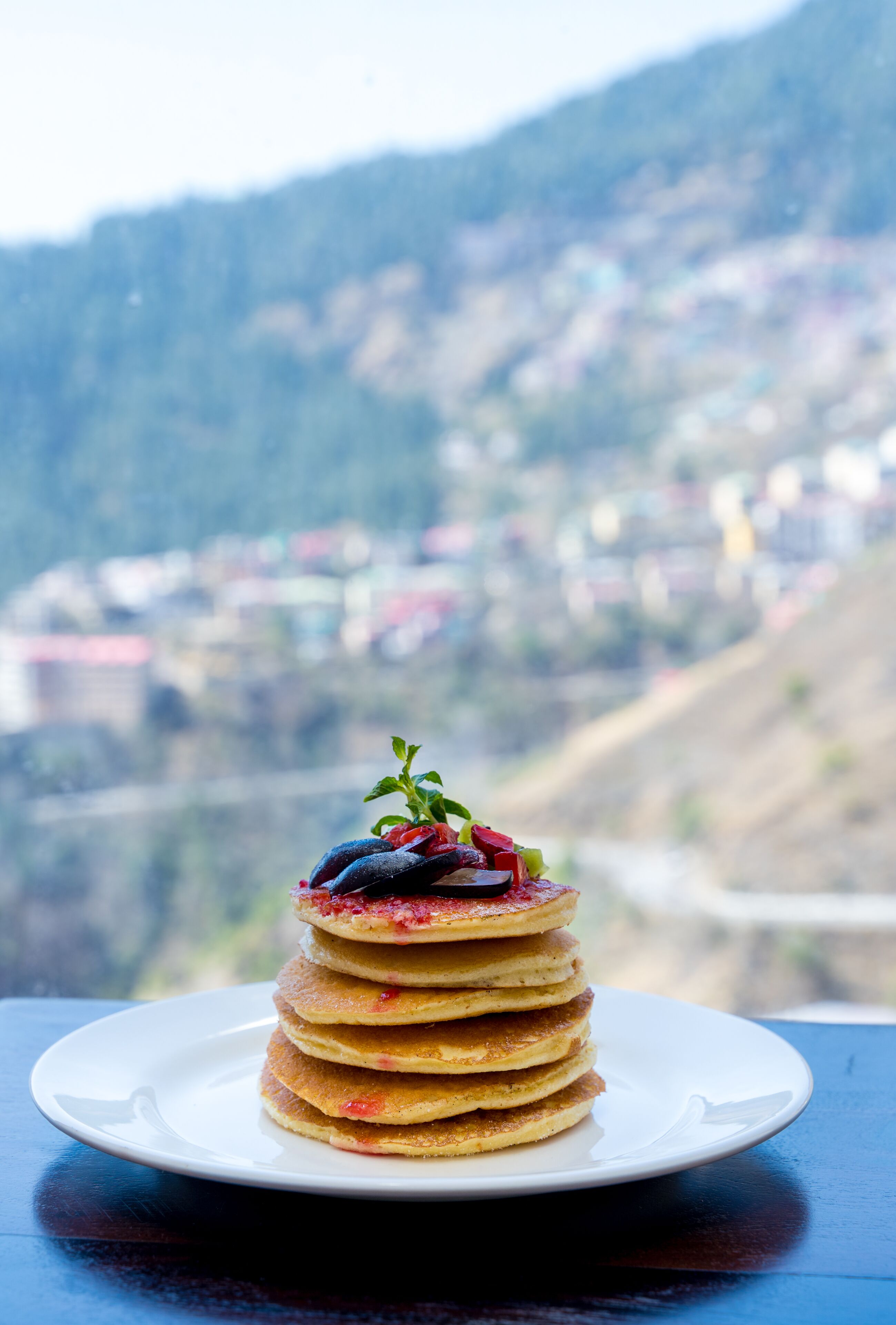 A stack of pancakes on a white plate with a scenic mountain view in the background.