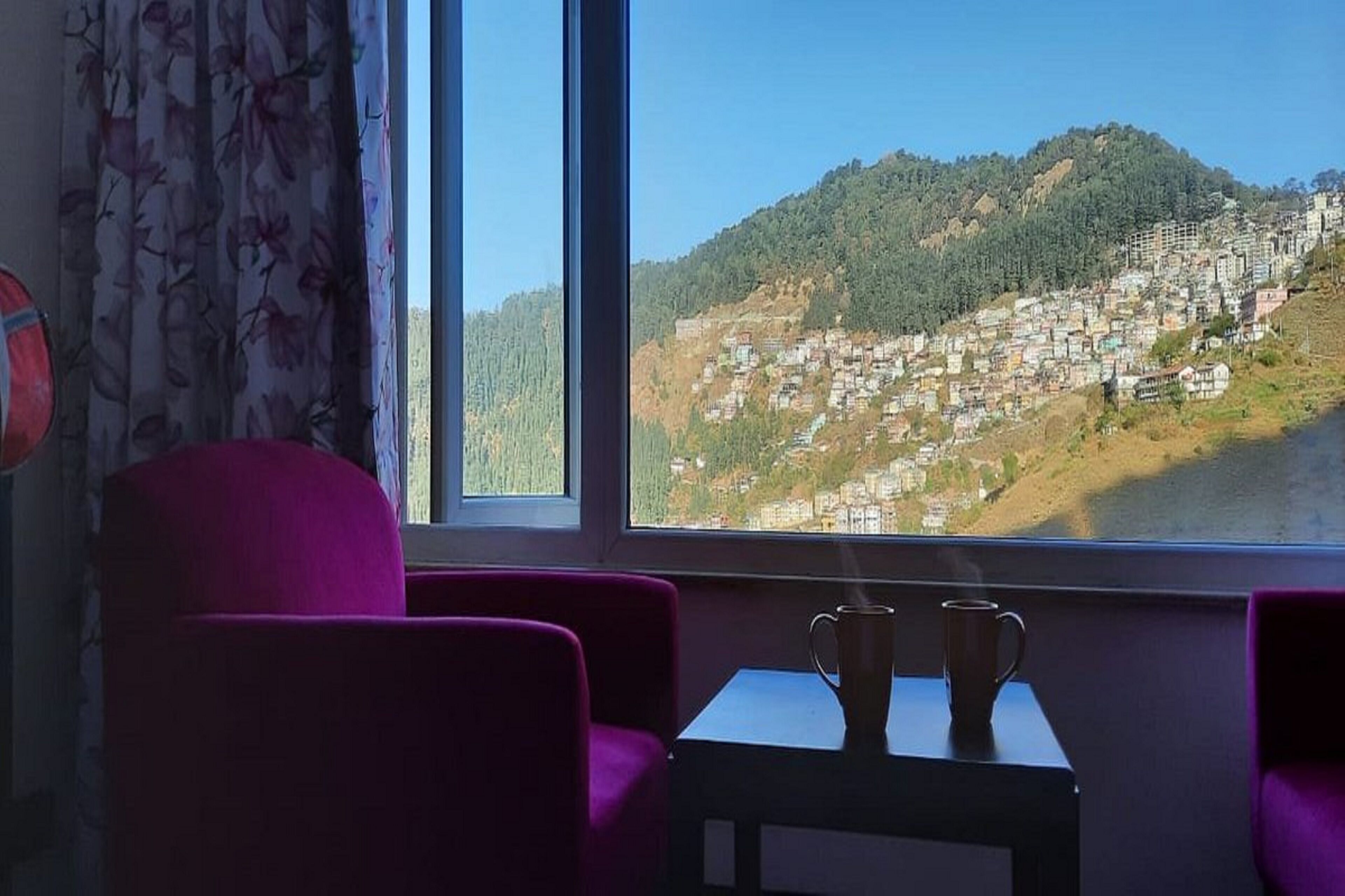 Una habitación con un ventanal que da a un poblado en la ladera de una colina.