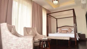 A bedroom with a four-poster bed, a sitting area with two armchairs, a small round table, and a large window with curtains.