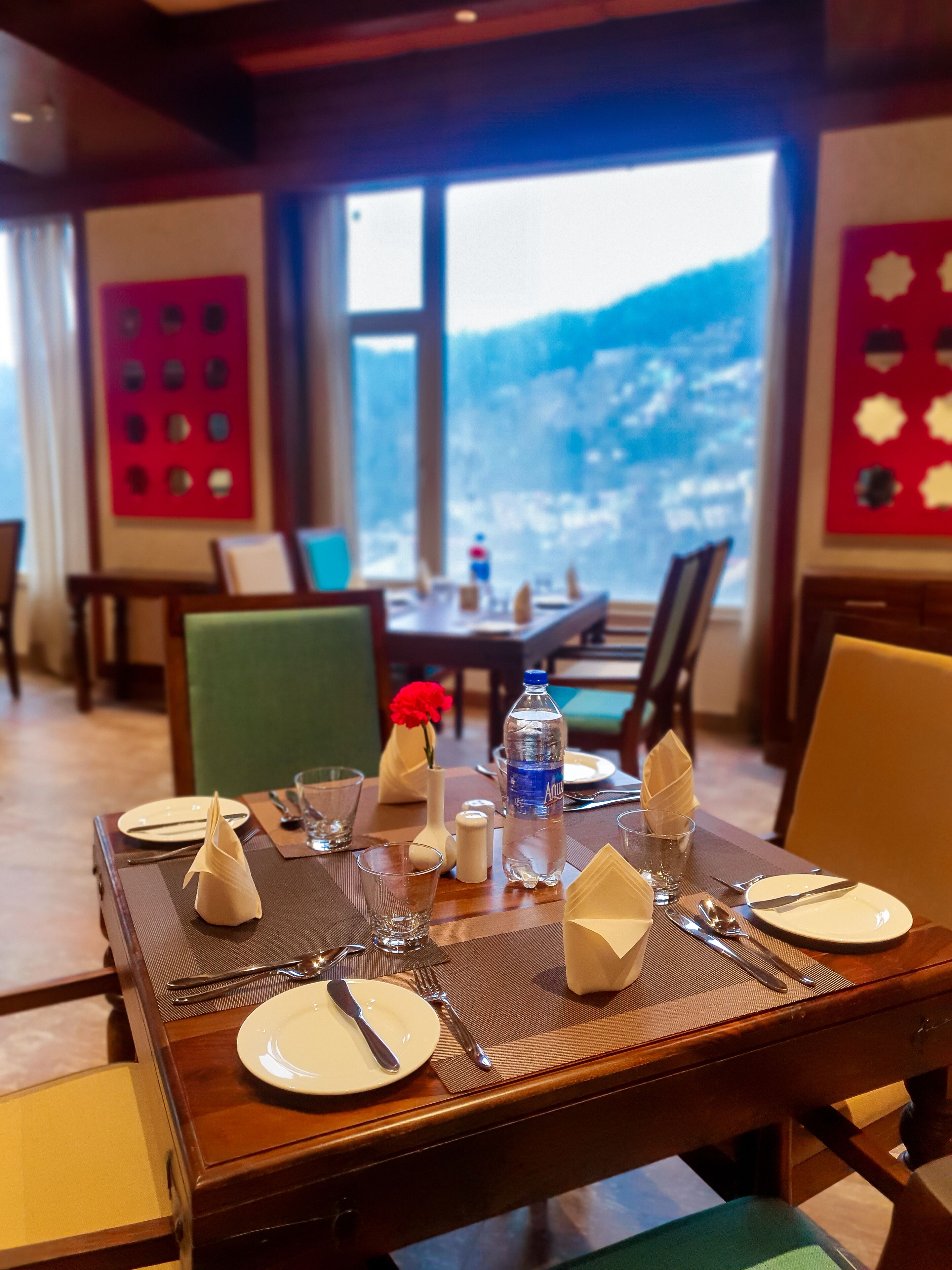 A dining table set with plates, cutlery, glasses, and a bottle of water, with a mountain view in the background.