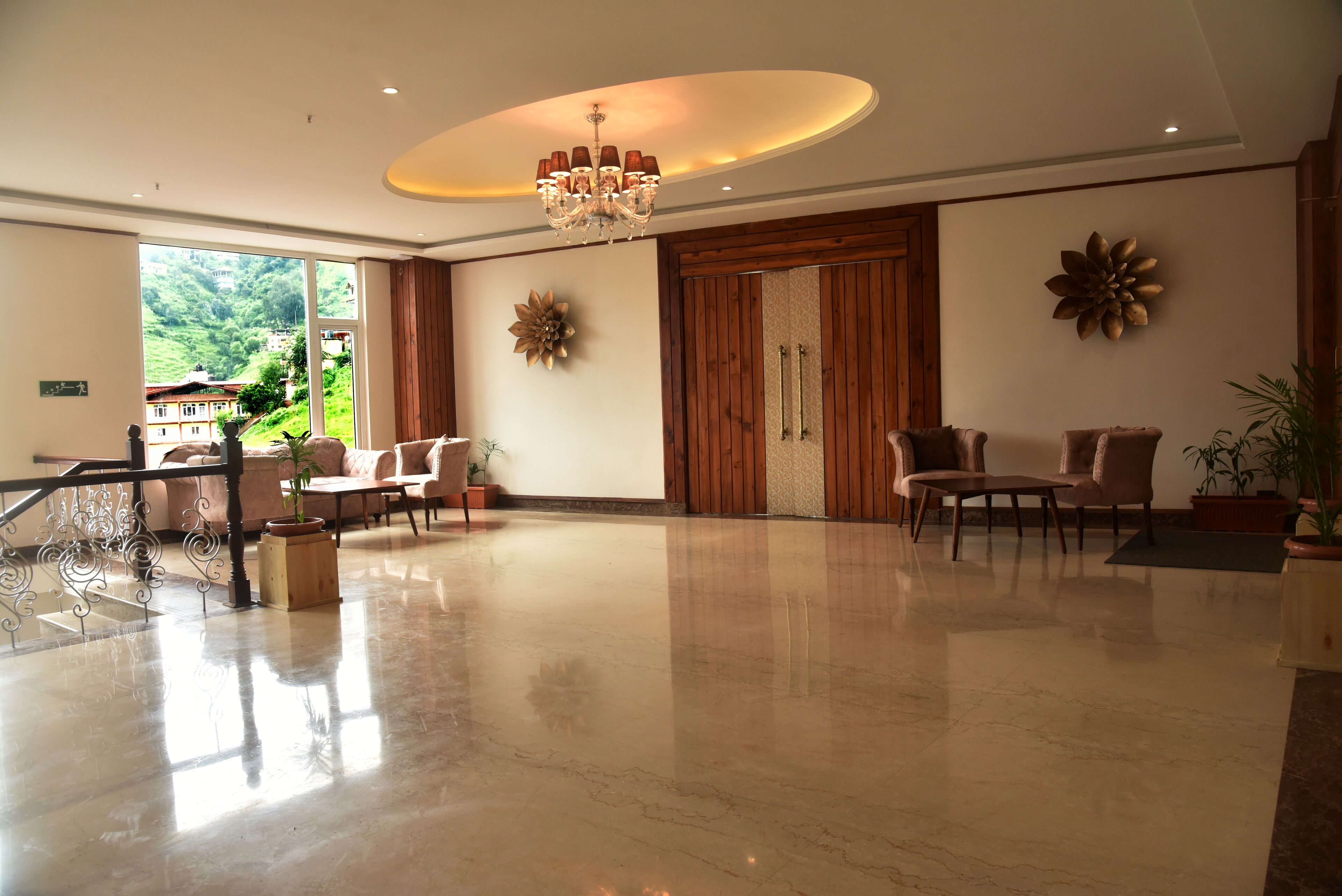 A spacious lobby with a chandelier, wooden paneling, and a large window offering a view of a hillside.