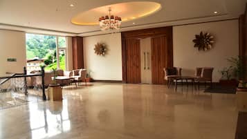 A spacious lobby with a chandelier, wooden paneling, and a large window offering a view of a hillside.