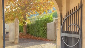 An arched entrance with a metal gate, a tree with autumn leaves, and a hedge in the background. - La Corte. A historic house at the gates of Bergamo. (Mozzo - (Bg))