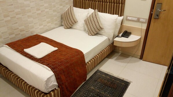 A hotel room with a bed, a bedside table with a phone, and a patterned rug.