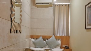 A hotel room with a bed, a nightstand, a mirror, an air conditioning unit, and a window with curtains. - Bentley Hotel Churchgate (Mumbai)