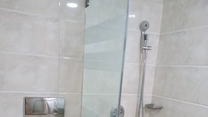 A modern bathroom with a glass-enclosed shower, a toilet, and a hand dryer. - Bentley Hotel Churchgate (Mumbai)