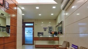 A reception area with a reception desk, a waiting area with striped chairs, and a glass display case. - Bentley Hotel Churchgate (Mumbai)