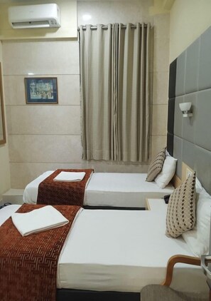 A hotel room with two beds, a picture on the wall, and an air conditioning unit.