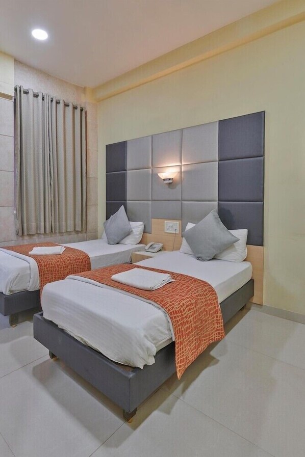 A hotel room with two single beds, a large padded headboard, a bedside table with a phone, and a curtain on the window. - Bentley Hotel Churchgate (Mumbai)
