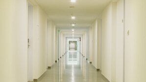 Un pasillo largo y estrecho con puertas a ambos lados, que da a una habitación luminosa al final.
