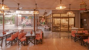Un restaurante con mesas y sillas de madera, lámparas de mimbre colgantes y un mural en la pared.